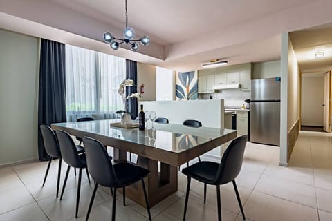 A well-lit dining area with a wooden table, dark chairs, and a view into an adjacent room
