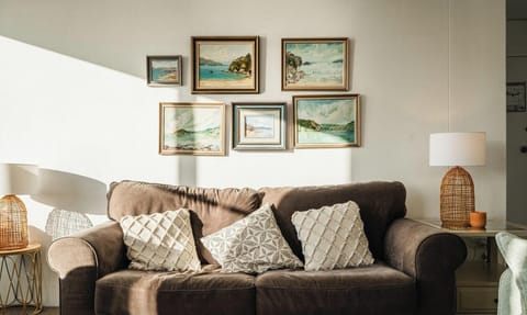 A comfortable dark brown sofa adorned with patterned cushions, set beneath an artistic gallery wall of framed landscape pictures.