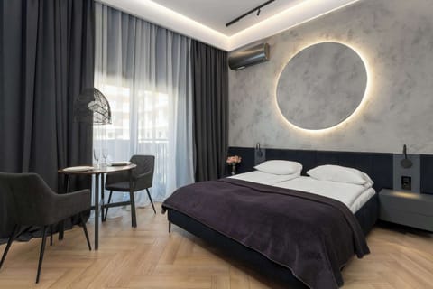 A stylish bedroom with a round illuminated wall feature above the bed. Floor-to-ceiling curtains frame the large window.
