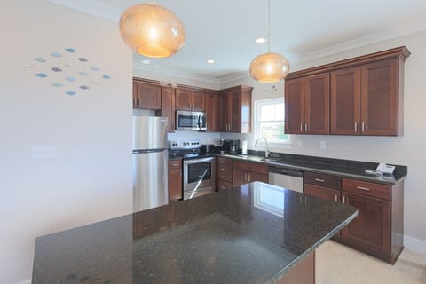 Modern kitchen featuring dark granite countertops, stainless appliances, Keurig and coffee maker, and stylish lighting