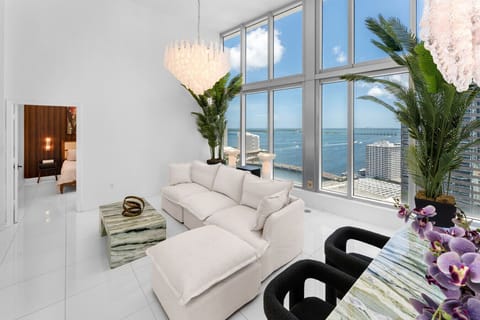 Cloud-like sectional with overfilled cushions faces a sleek stone coffee table and a picture frame that magically transforms into a hidden 55-inch smart TV with all major streaming services, set against breathtaking city views.