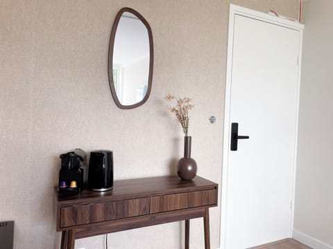 Cozy design featuring a light wood table, dark vase, and mirror against a textured beige wall.