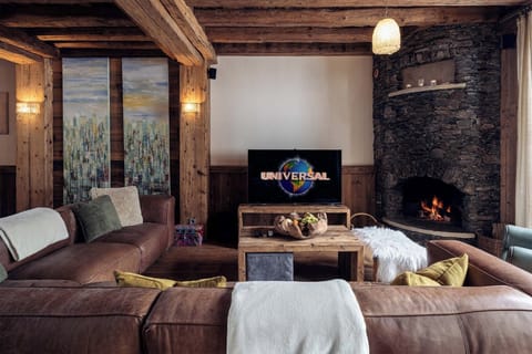 Experience cozy luxury in the panoramic living room, featuring bespoke alpine décor, a stunning stone fireplace, and plush seating ideal for relaxation and entertainment.