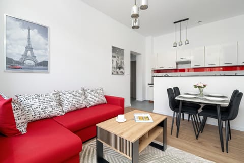 A bright living room with a red sofa bed, wall art, and a modern coffee table. The space is designed for both relaxation and social gatherings.