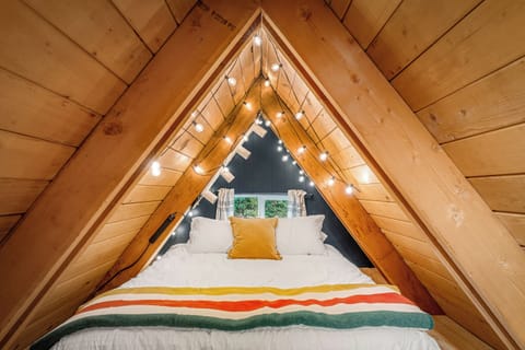 Cozy A-frame loft nook with a comfy queen bed and twinkle lights.