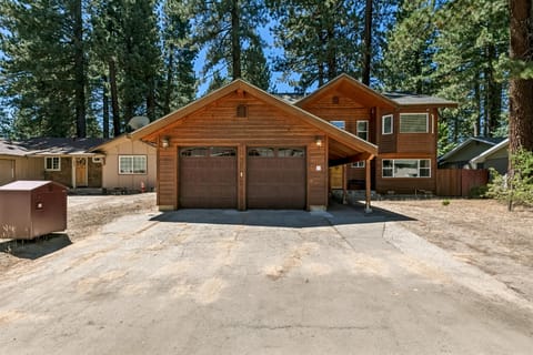 Exterior view of the wood-paneled house with a double garage and tall pine trees surrounding the property.