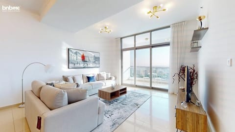 Bright &amp; Spacious Living Room with Balcony Access, Unwind in this sunlit living space featuring plush sofas, modern décor, a smart TV, and floor-to-ceiling windows that open to a private balcony with partial sea and city views—perfect for relaxation.
