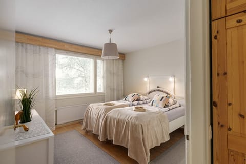 Bright and cozy bedroom featuring two single beds pushed together to form a large sleeping space. The room is decorated with soft, neutral tones and colorful pillows for a welcoming atmosphere.