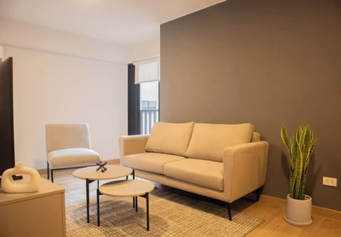 A cozy sitting area with a beige sofa, armchair, small table, and a plant, set against a grey accent wall.