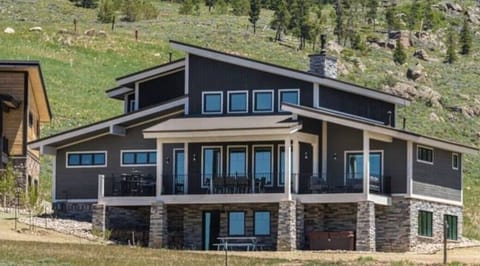 Modern mountain retreat featuring stone and wood architecture with expansive decks overlooking natural hillside terrain.