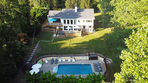 🏡 Stunning aerial view of a spacious modern home with expansive decks, multiple outdoor seating areas 🪑☀️, private hot tub ♨️, and a fenced-in pool 🏊‍♂️ surrounded by lush greenery 🌳🌿—perfect for relaxing and entertaining.