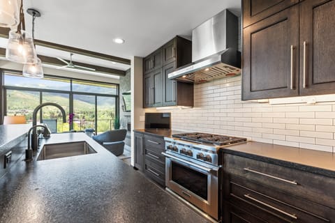 The kitchen with dark wood cabinets, white backsplash and stainless steel gas range.