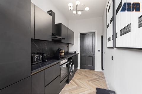 Fully equipped kitchen featuring a sleek black countertop, washing machine, stovetop, oven, fridge, and essential cookware—ideal for home-cooked meals during your stay.