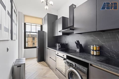 Fully equipped kitchen featuring a sleek black countertop, washing machine, stovetop, oven, fridge, and essential cookware—ideal for home-cooked meals during your stay.