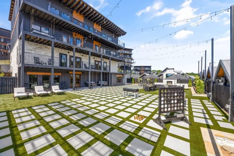 Spacious outdoor lounge area with modern turf and pavers, string lights, lounge chairs, oversized games, and shaded seating—perfect for entertaining or relaxing under the sun in a resort-style environment.
