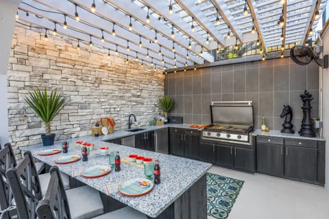 Covered outdoor kitchen and grilling station with granite countertops, stainless steel grill, and bar seating. Ideal for BBQ nights, complete with festive string lights and upscale design touches that elevate your alfresco experience.