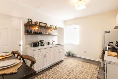 Fully equipped kitchen featuring a refrigerator, sink, stove, toaster, coffee maker, salt and pepper, olive oil, microwave, and essential cooking supplies. A bar table seats two, perfect for shared meals. Handcrafted rustic floating shelves, vintage touch