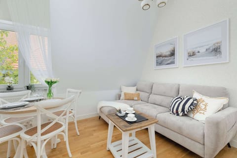 A bright living room with a light sofa and a round glass table. White walls and natural light create an airy atmosphere.