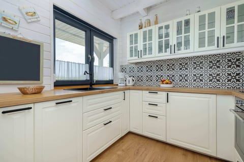 A modern kitchen with cream-colored cabinets, black countertops, and large windows.