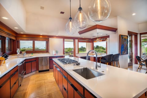 Your gourmet kitchen features gleaming countertops, professional appliances, and stunning pendant lighting, perfect for cooking while enjoying tropical views.