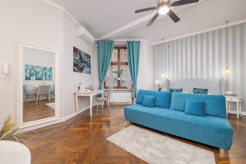 A bright living room with a blue sofa and modern decor on the walls. The space features warm wooden flooring and a ceiling fan for comfort.