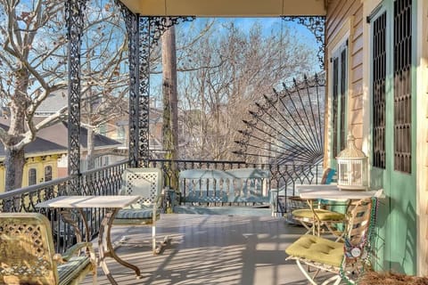 This shared balcony stretches long and narrow, drawing the eye toward its ornate wrought-iron railings and intricate corner panels. The perspective highlights depth and openness, with seating areas creating an inviting, elevated view of the street.