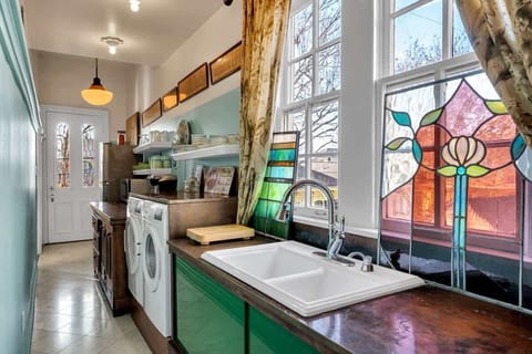 Charming galley kitchen with copper countertops, open shelving, and washer/dryer. A large window with colorful stained glass adds character and natural light to this bright, functional space.