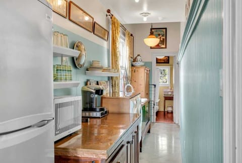 Charming galley-style space with vintage details, featuring open shelving, a coffee station, microwave, and copper countertop. A washer and dryer add convenience, with natural light flowing in toward the bathroom at the end of the hall.