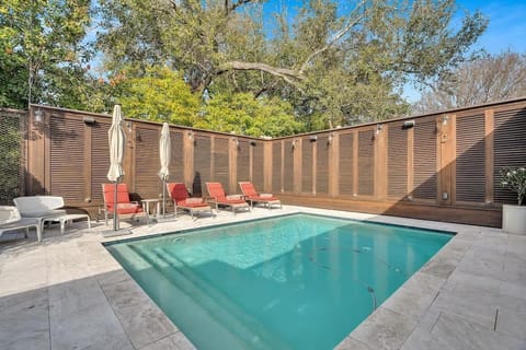 Sunny poolside retreat with cushioned loungers, umbrellas, and privacy fencing, offering a serene setting for relaxation surrounded by lush greenery.