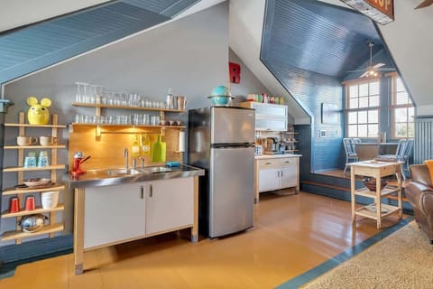 Bright and functional kitchenette with stainless-steel sink, open shelving, and modern appliances, complemented by a cozy elevated dining nook with natural light and charming wood finishes.