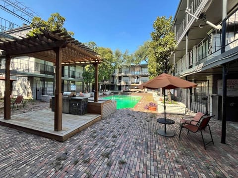 Community outdoor lounge with shaded seating, BBQ grill, and poolside relaxation area. A perfect spot to gather, cook out, or unwind under the pergola.