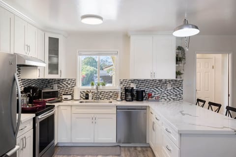 Modern kitchen with white cabinets, stainless appliances, and mosaic backsplash.