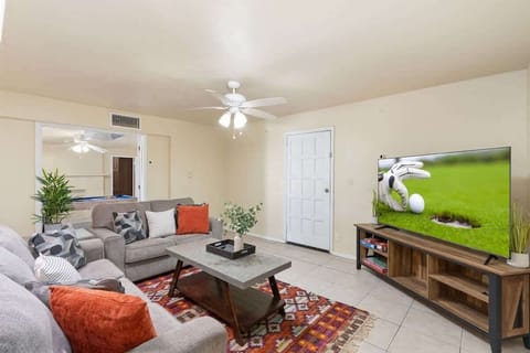 Relax on the gray sofa and enjoy a movie on the large TV across the room. A patterned rug, wood coffee table, and pops of orange pillows add warmth, while the ceiling fan keeps the space comfortable for laid-back evenings in.