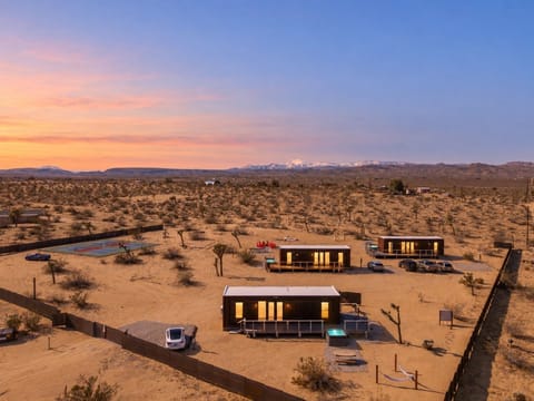 Three private desert retreats beneath a glowing Joshua Tree sunset, each with its own hot tub and plunge pool, plus double pickleball courts and endless mountain views.
