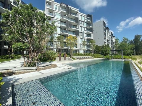 Outdoor swimming pool surrounded by greenery and modern buildings.