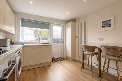 Bright modern kitchen with cream cabinets, gold faucet, breakfast bar, and door leading to rear garden.