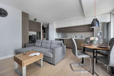 A bright living room with a comfortable gray sofa and a wooden coffee table. The open kitchen and dining area make the space perfect for gatherings.