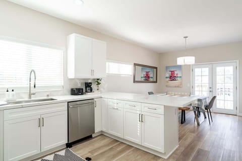 This kitchen and dining space blends modern elegance with coastal charm. The dining area features a contemporary chandelier and bright artwork, adding a pop of color and personality. Plus, those French doors bring in plenty of natural light!