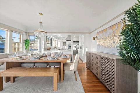 Natural wood finishes create a warm, earthy vibe, while a richly detailed buffet table adds character to the space. White walls and ceiling allow the expansive windows to flood the room with natural light, making it feel bright and airy.