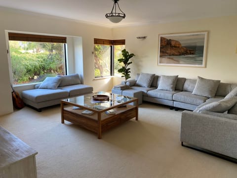 Downstairs living area looking out over front garden with 8 seater couch, smart TV and sound system