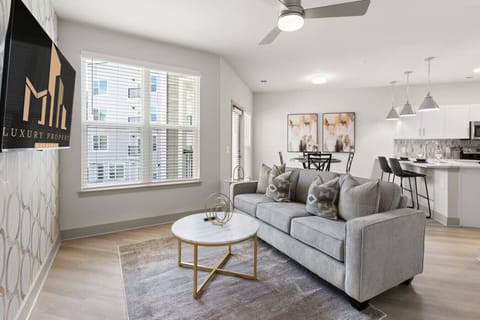 Modern Living Room-Bright and stylish living space with a sleek grey sofa, gold-accent coffee table, and smart TV. Open layout flows into the dining and kitchen area, perfect for relaxing or entertaining.
