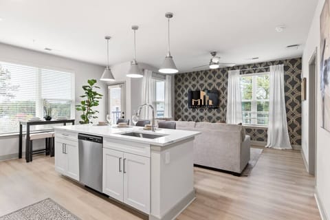 Modern Open-Concept Living-Bright open layout with sleek kitchen island, stainless steel appliances, and cozy living area. Stylish accent wall, natural light, and warm flooring create a welcoming space for dining and relaxation.