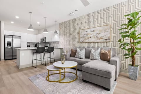 Open-Concept Living – Stylish lounge with a plush sectional, marble-top nesting tables, and bold accent wall. Flows seamlessly into the modern kitchen with bar seating, perfect for both relaxation and entertaining.