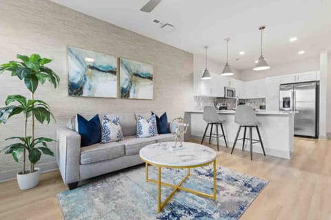 Modern Open-Concept Living-Bright and stylish living room with plush seating, abstract art, and natural accents flows seamlessly into a sleek kitchen with stainless steel appliances and breakfast bar seating.