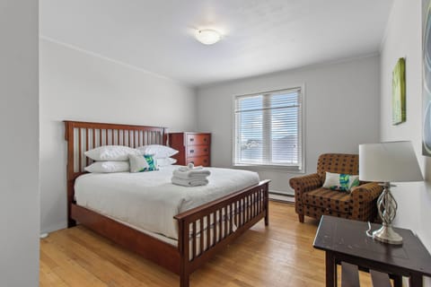 Relax in this bright bedroom featuring a queen-sized wooden bed frame, hardwood floors, and large windows for plenty of natural light.