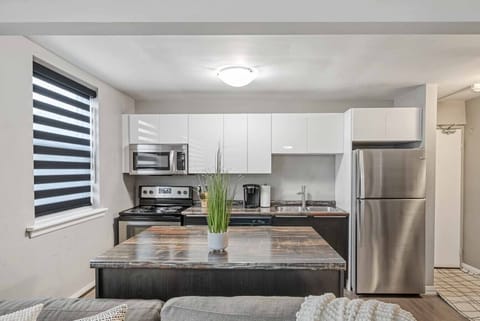 Cook and dine in our modern, fully equipped kitchen! Features a spacious island with a plant, stainless steel appliances including a fridge, stove, oven, microwave, and dishwasher. Enjoy ample storage, a coffee maker, and stylish window blinds for a brigh
