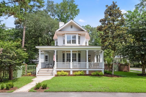 Traditional two-story house with white siding, wide porch with rocking chairs, and lush green lawn.