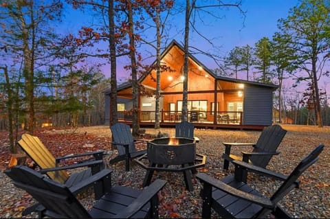 Modern cabin with fire pit seating surrounded by tall pines at sunset
