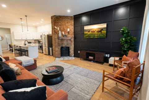 Sink into the burnt orange sectional sofa while admiring the dark modern accent wall and the rustic exposed brick column. The open layout keeps the conversation flowing right into the kitchen space.