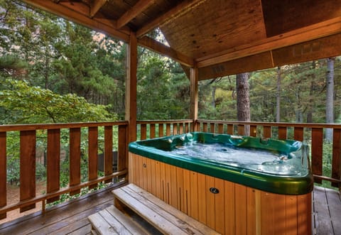Relax in the hot tub on a covered deck surrounded by tall pines.